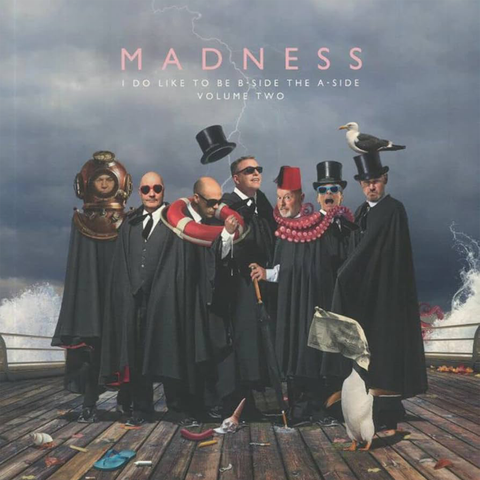 Madness Band Members in black robes on a jetty with water splashing behind them