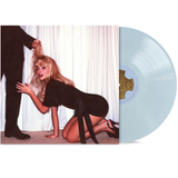 Sabrina in a black dress kneeling on the floor with a man's leg in front of her, against a white curtain background with blue vinyl out of sleeve