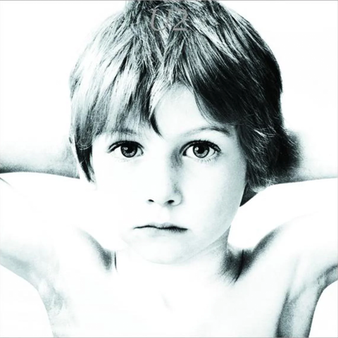 A high-contrast black and white close-up portrait of a young child with short hair, looking directly at the camera.