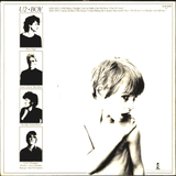 The back cover of the U2 - Boy album, featuring a large black and white portrait of a young boy on the right and four smaller black and white portraits of the band members on the left, with tracklist text at the top.