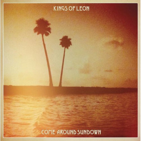 A serene beach scene at sundown, with two distinct palm trees standing against a golden-hour sky.