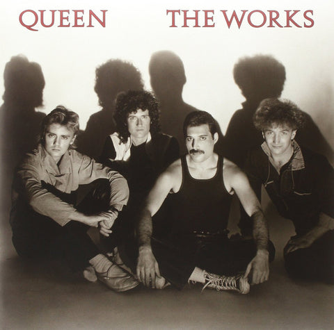 A black and white cover of the rock band Queen for their album 'The Works', featuring the band members seated close together with a dark, moody atmosphere.