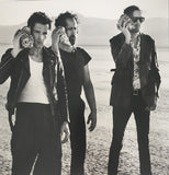 3 Band Members holding sea shells to their ears in a desert setting